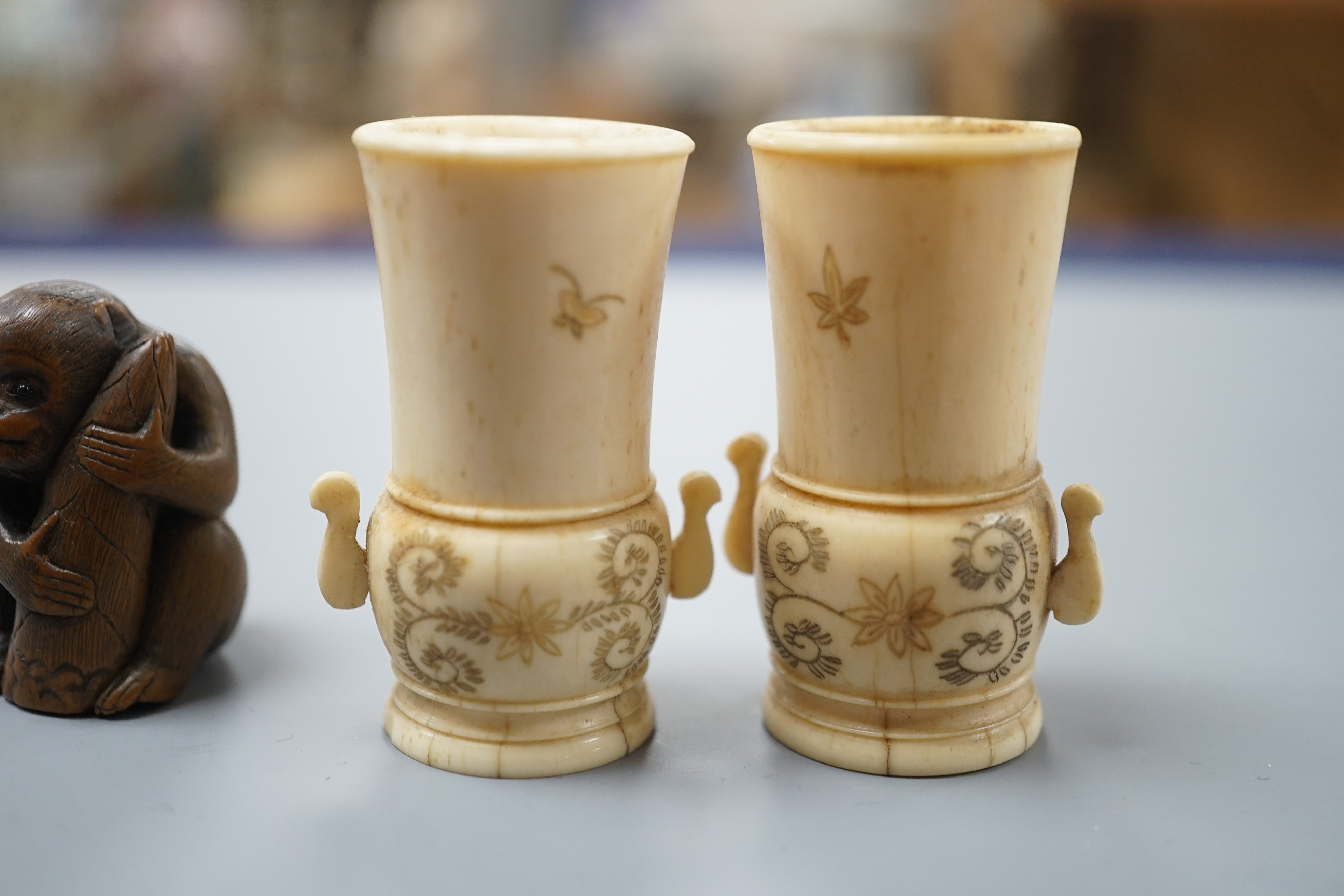 A pair of early 20th century Japanese miniature ivory vases, 5.3 cm, engraved with a lady and a wood netsuke in the form of a monkey holding a bamboo shoot (3)